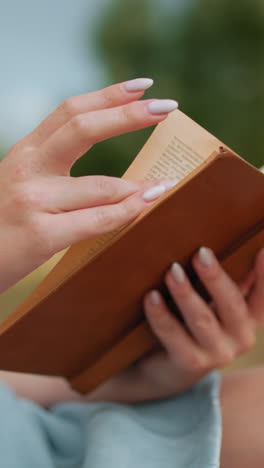 primer plano de una mujer leyendo un libro viejo al aire libre, volviendo delicadamente las páginas con manos bien cuidadas, enfoque suave en pantalones cortos azules, fondo natural borroso