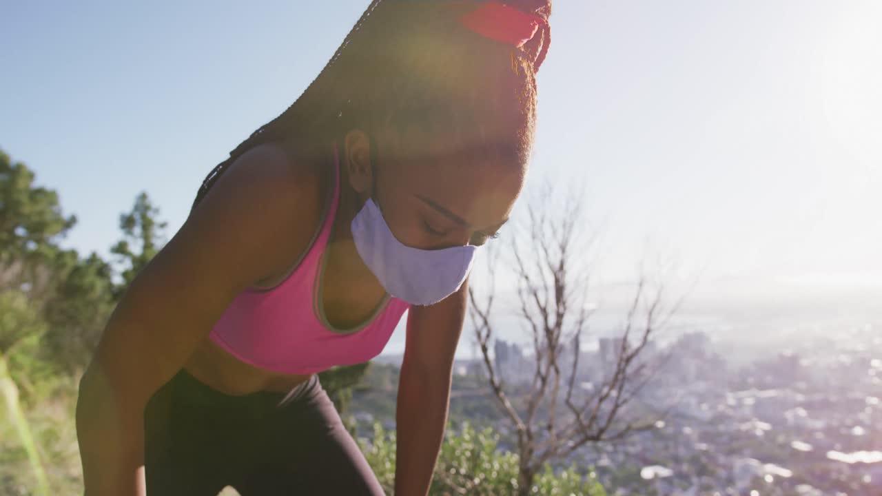 Tired african american woman wearing face mask taking a break from running outdoors