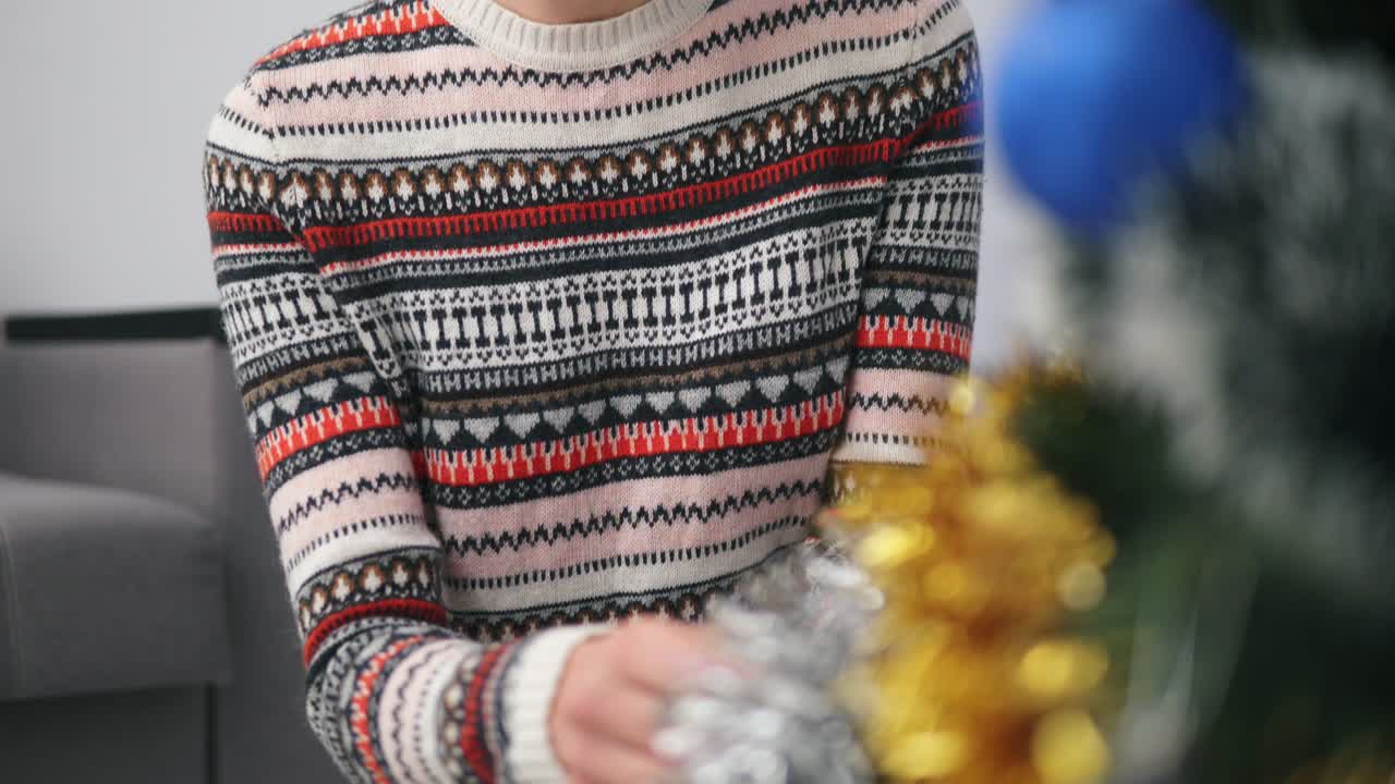 Closeup view of woman's hands decorating a Christmas tree with toys in modern appartment. Shot in 4k
