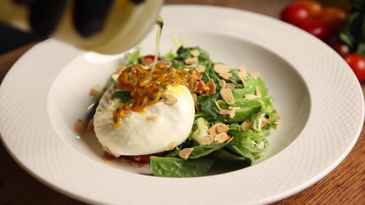 Pouring Dressing on a Fresh Burrata Salad with Avocado and Passion Fruit