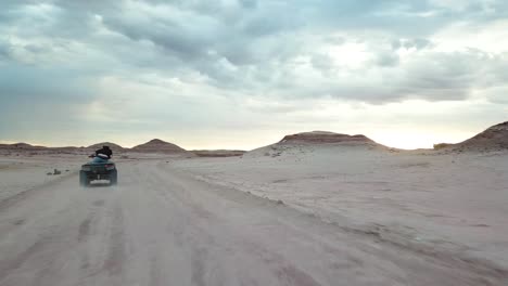 vista aérea de tipo de acción dinámica del hombre que conduce un vehículo quad atv en una carretera polvorienta del desierto bajo un cielo tormentoso