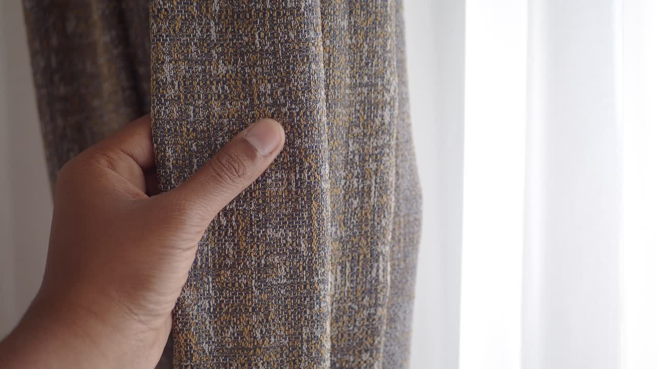 밝은 창문 근처에 회색과 노란색 패턴의 커튼을 열고 있는 손의 가까운