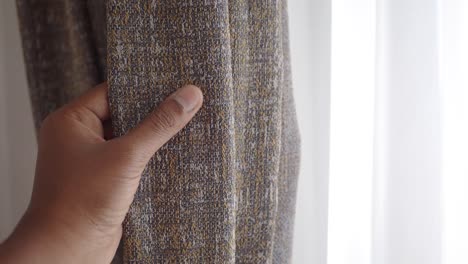 close up of a hand opening grey and yellow patterned curtains near a bright window