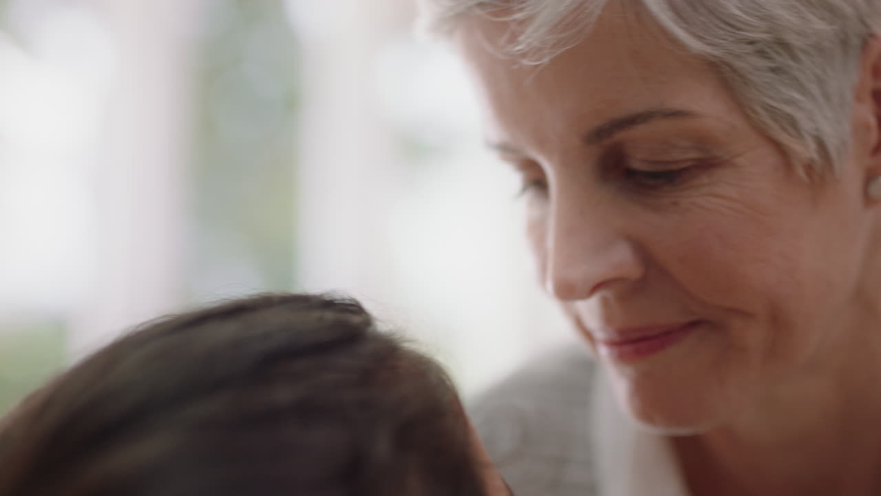 행복한 할머니는 작은 소녀를 이마에 부드럽게 키스하고 손녀에 대한 사랑을 보여주고 자랑스러운 할머니는 집에서 손자에 대한 애정을 나누고 있습니다.