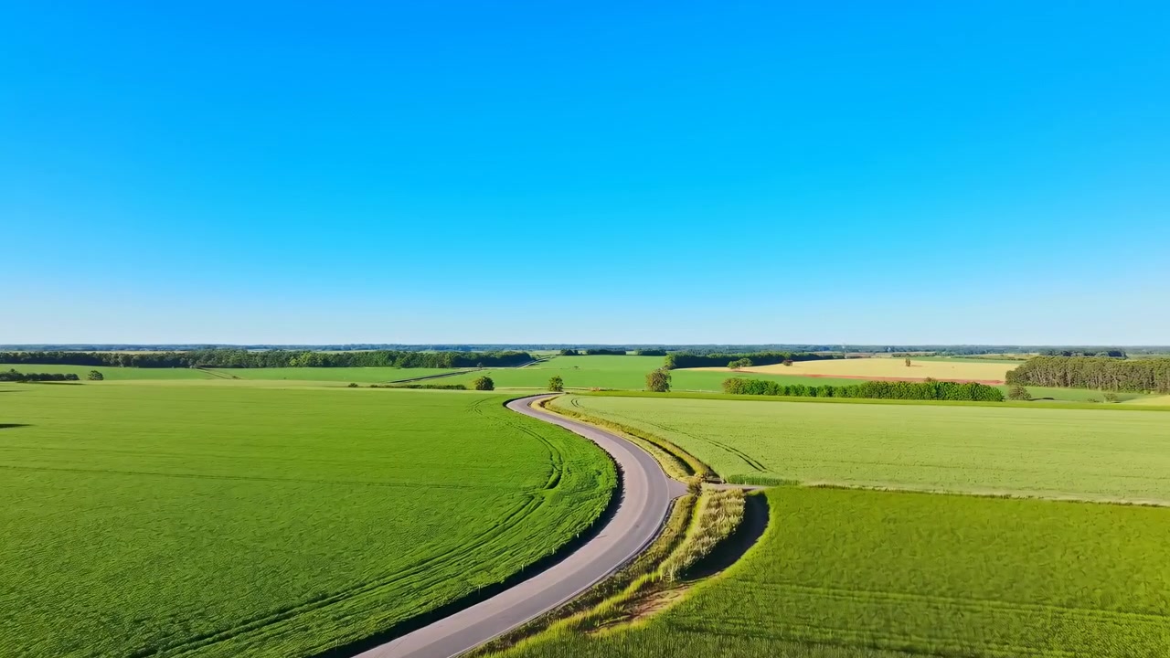 Winding Country Road Through Green Fields Under Clear Blue Sky, Drone Captures Sweeping Curve, Sunlit