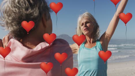 animation of red heart balloons, over women exercising on beach