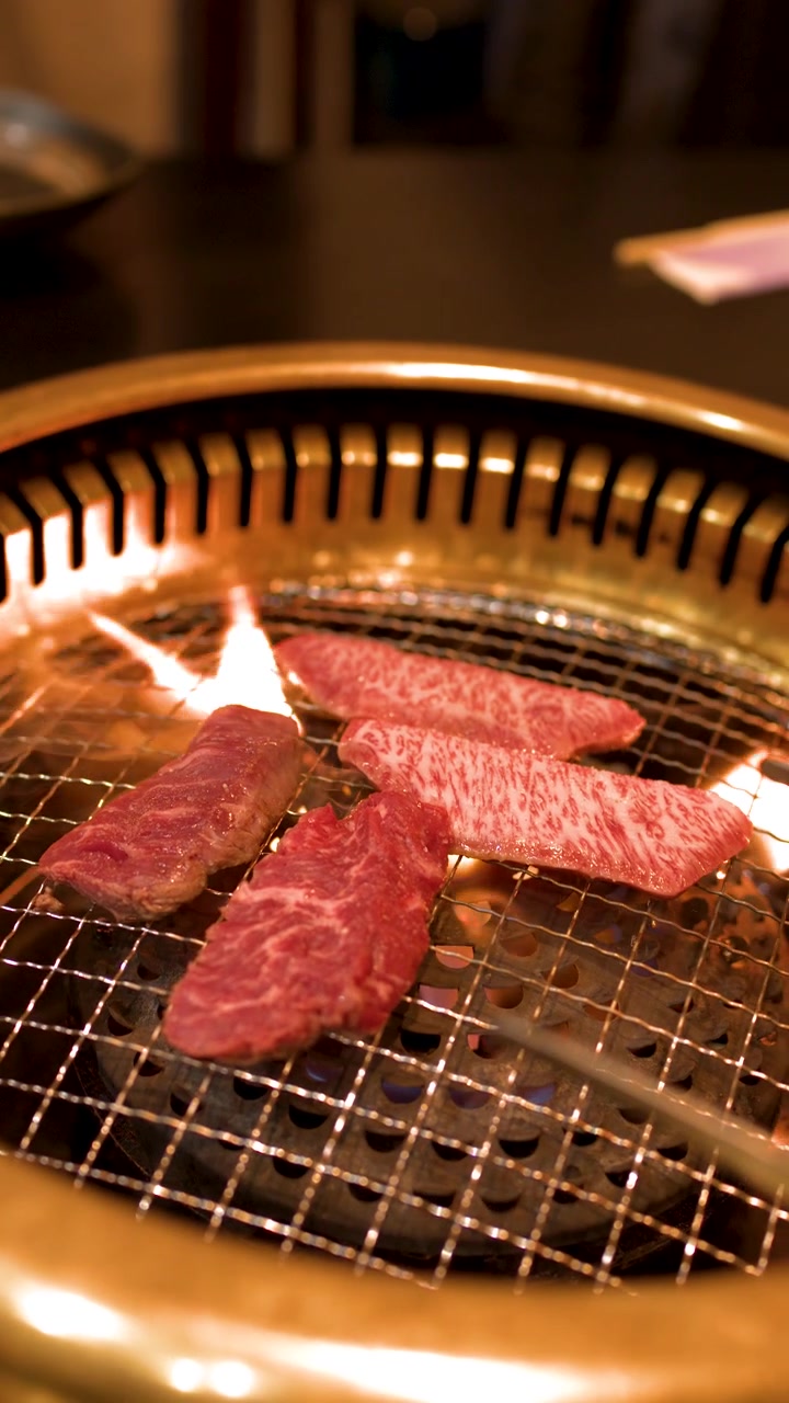 Primo piano di pregiata carne di manzo marmorizzata che cuoce su una griglia metallica circolare con fiamme vive