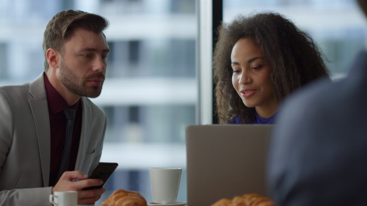 una pareja multiétnica de hombres de negocios sentados usando una computadora portátil en la oficina de un café.