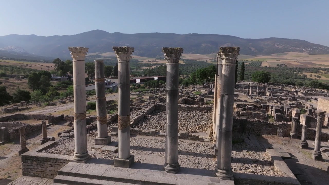 Vista da drone a bassa quota delle monumentali colonne del Campidoglio presso il sito archeologico di Volubilis, patrimonio mondiale dell'UNESCO in Marocco, che domina l'antica città romana e le montagne di Zerhoun