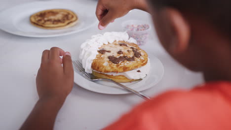 cerca de un niño añadiendo salpicaduras a panqueques con cara hecha de crema y salsa de chocolate en la cocina