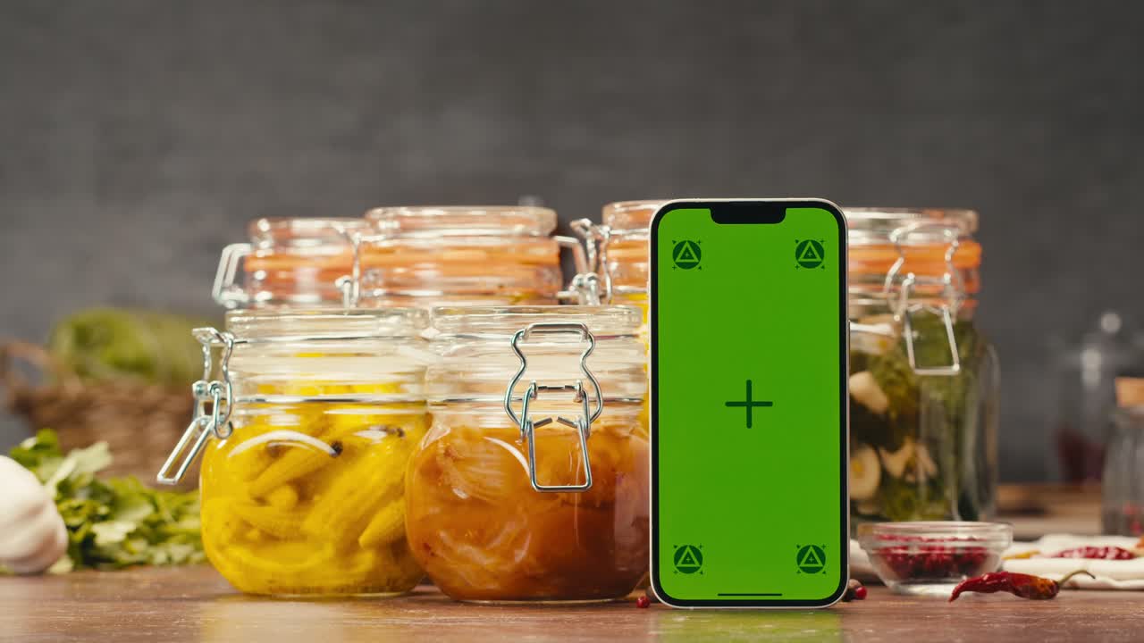 A modern greenscreen mobile device is displayed on a wooden table next to a bowl of food, demonstrating its versatility for multimedia projects