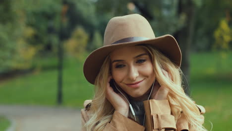 close-up view of caucasian young blonde woman putting the headphones on and listening to the music while walking in the park in autumn