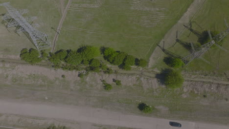 aerial tracking shot of a black suv driving along a dirt road below electrical pylons