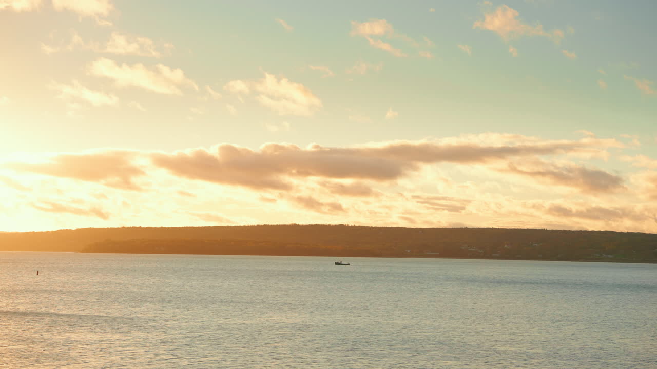 Static shot of golden hour sunset at the seaside. View of the coastline in the distance. Warm colorful sky, Fluffy clouds.