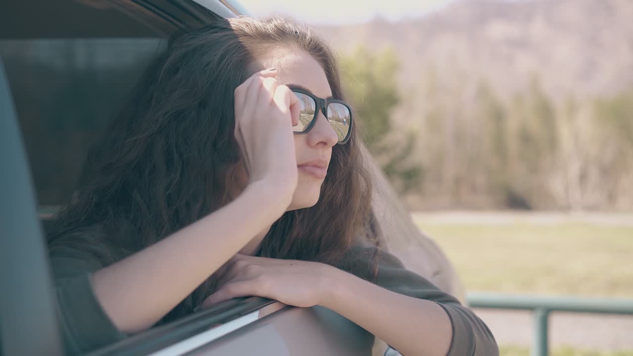 relaxed young lady in grey blouse leans out of modern car