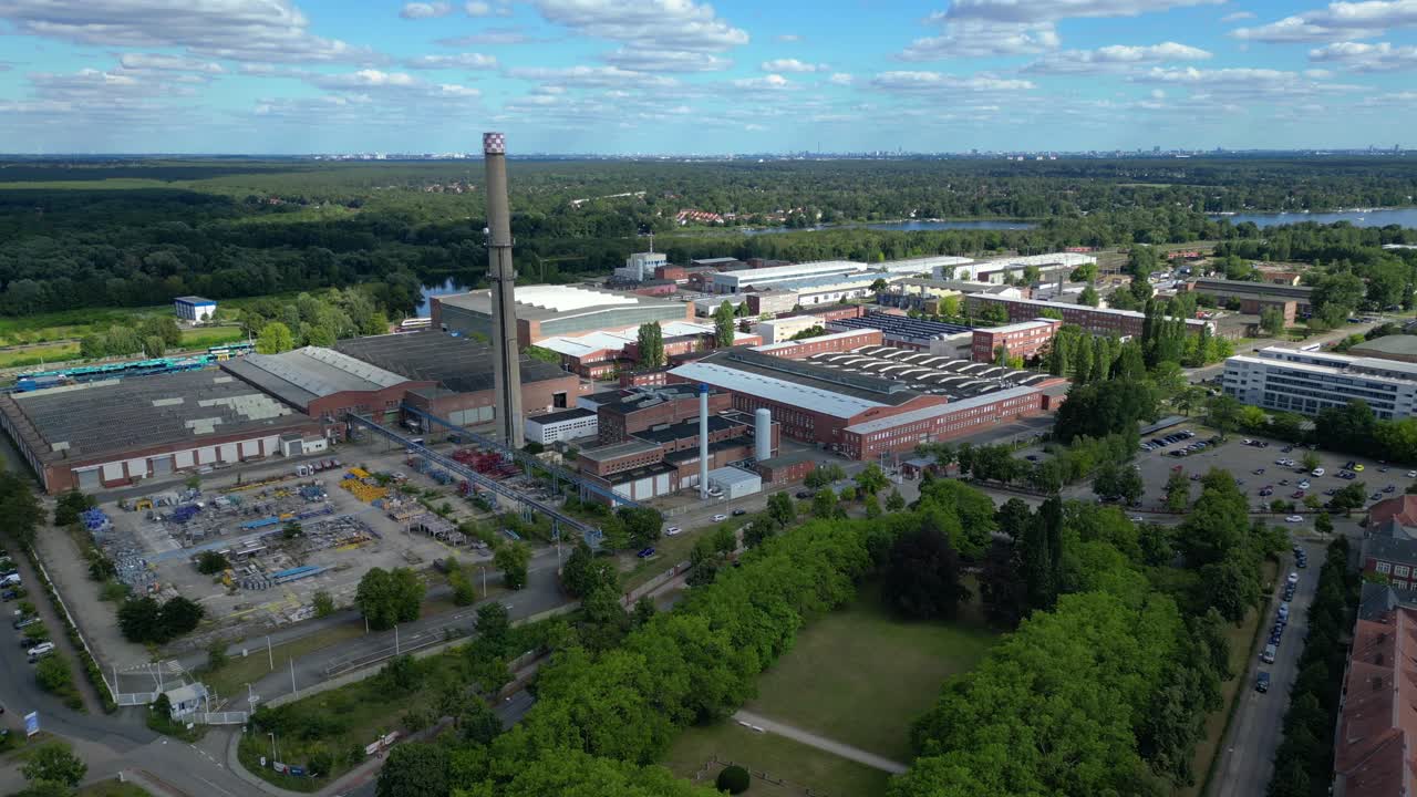 Hennigsdorf industrial area with modern offices, old factory buildings and chimneys under blue sky. Magic aerial view flight static tripod hovering drone