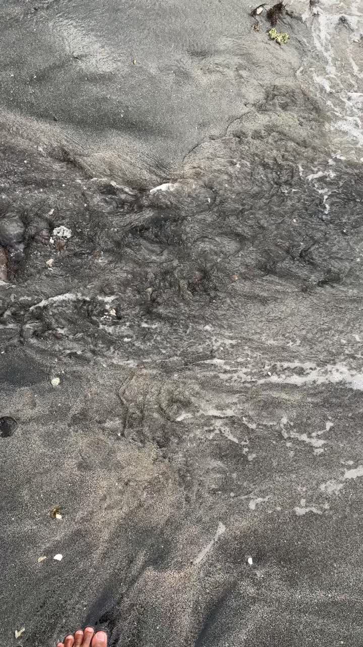 Onde dell'oceano che si ritirano su una spiaggia di sabbia scura