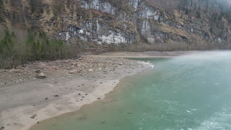 Aerial-orbit-around-connection-of-river-and-reservoir-entrance-at-base-of-steep-cliff-with-clay-silt-deposits-on-shoreline