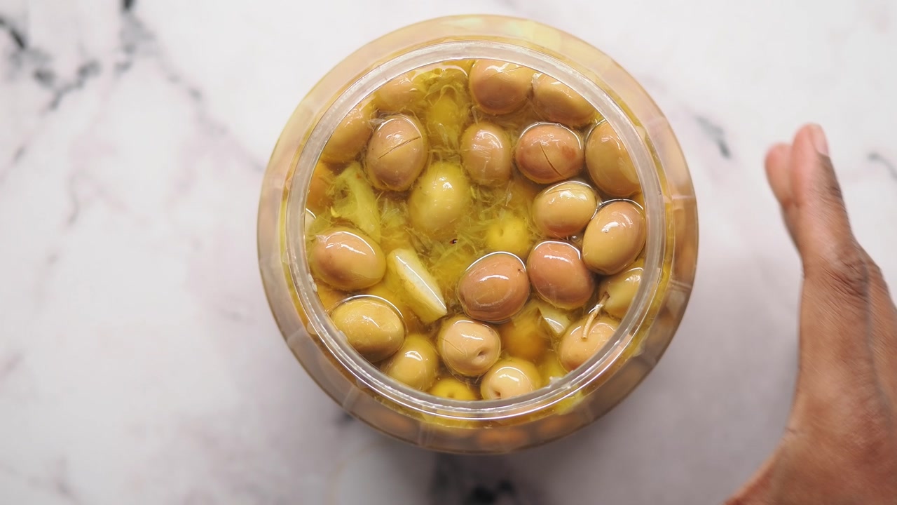 Hands Opening a Jar of Green Olives with Garlic