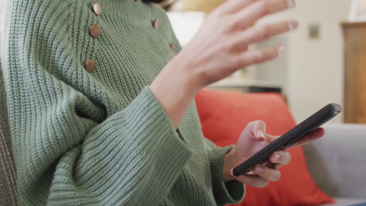 두 인종의 여성이 미소 짓고 거실에서 스마트폰을 사용하고 있습니다.