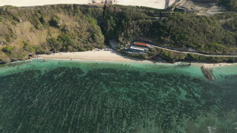 secluded beach at bottom of uluwatu cliffs looks out over blue lagoon drone track left 4k 60fps
