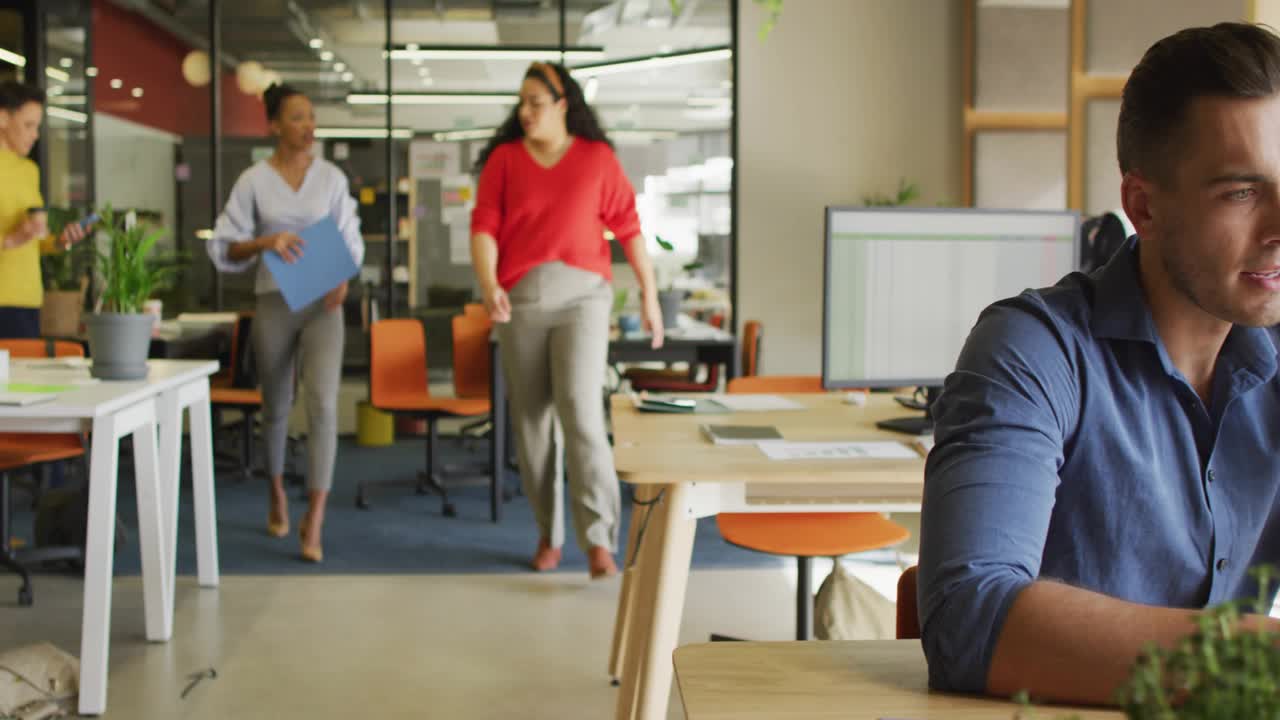 Male speaking into smartphone as team passing by, social alerts floating around business desk