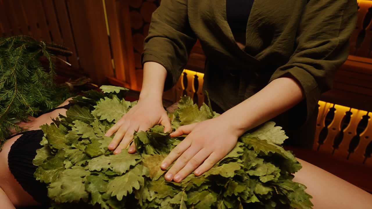 Woman receiving a banya treatment with oak leaves