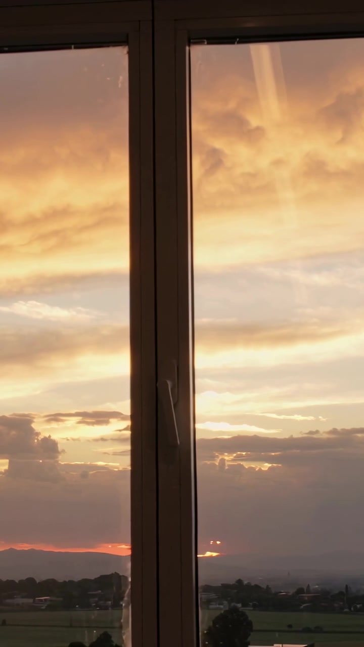 Video vertical: Cámara panorámica mostrando una ventana de dos paneles que enmarca un atardecer sobre campos, con el pomo brillante.