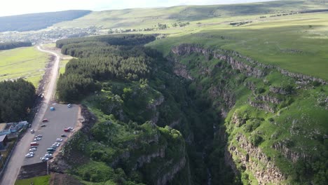 Aerial-shot-of-valley-surrounded-by-mountains-country-road-car-passing-through-forest-meadows