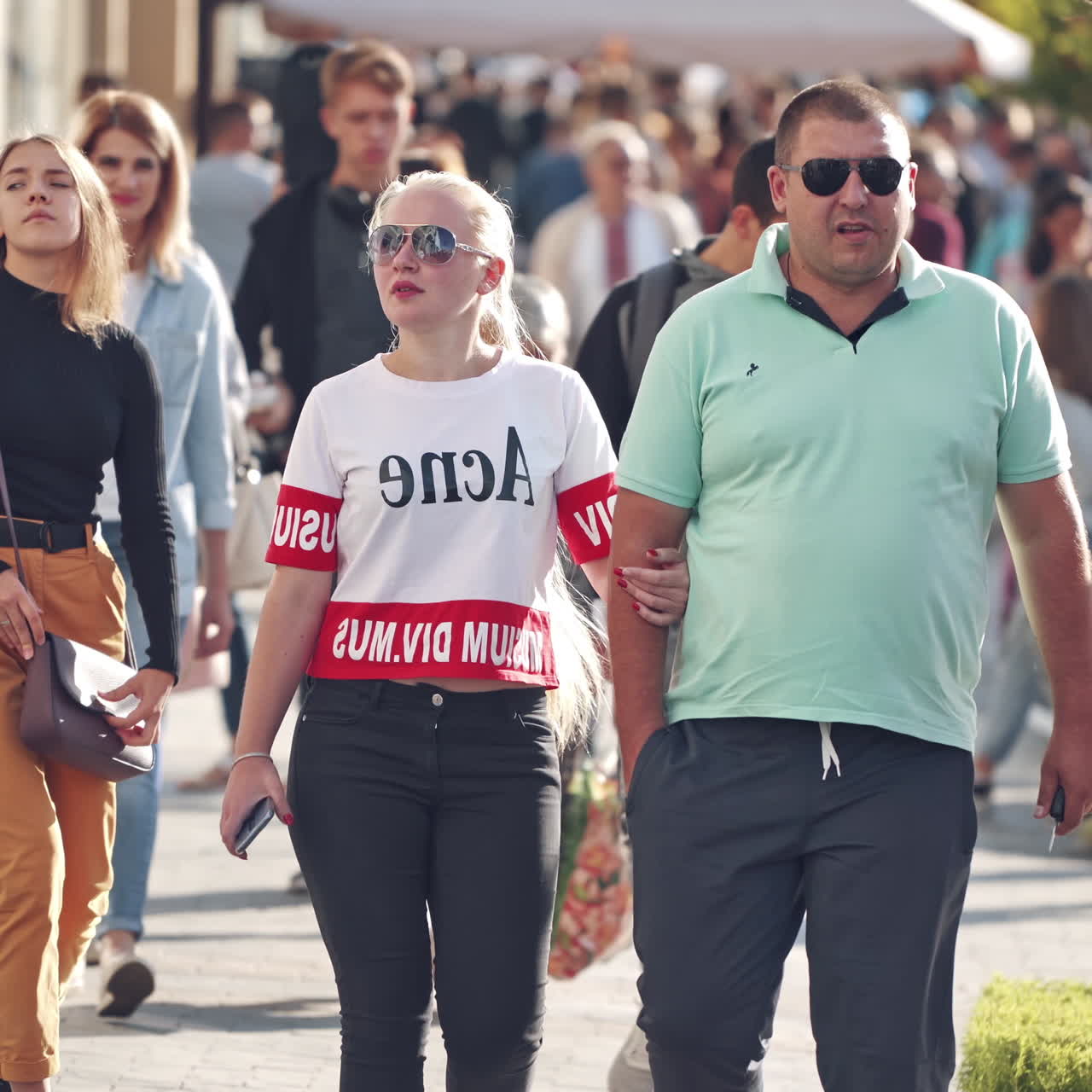 People walking along the street. Urban life scene. Crowded sidewalk with pedestrians in summer day.