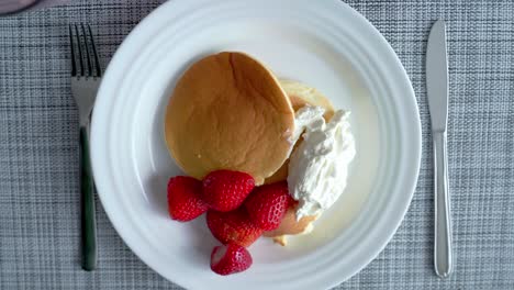 cerca de la mano sirviendo panqueque con fresa y crema batida en el plato en casa al mediodía directamente desde arriba