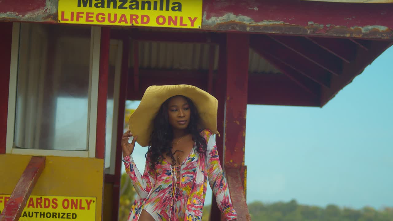 한 소녀가 밀짚모자와 섹시한 비키니를 입고 구조대 부스에 서 있다