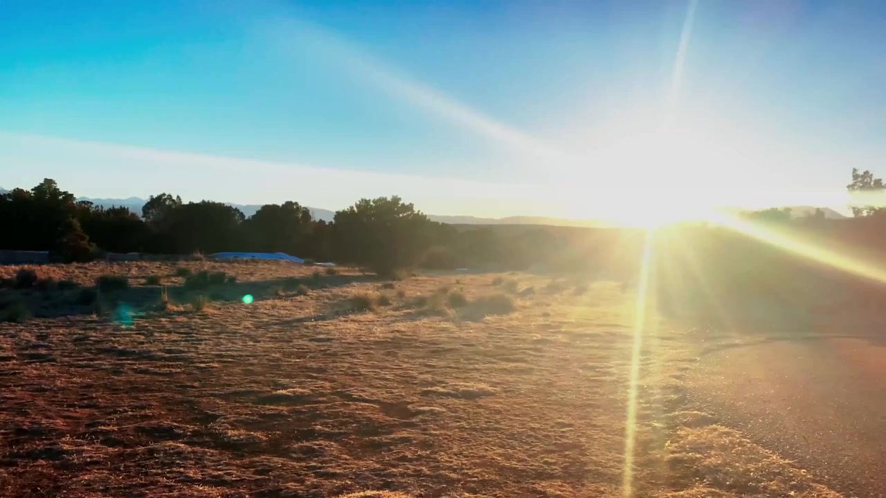 Il sole splendente tramonta proiettando ombre drammatiche e lunghe su un paesaggio montuoso di arbusti aridi con cieli azzurri e sereni