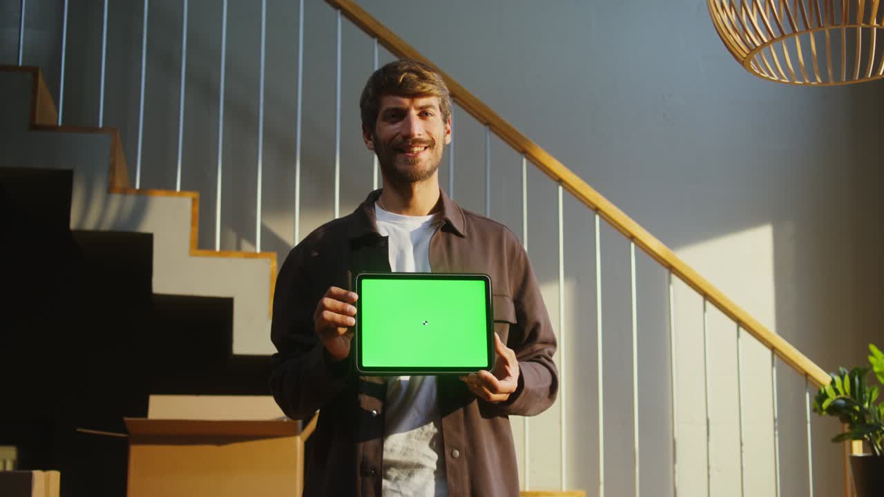 un hombre sonríe mirando a la cámara y sosteniendo una tableta con una pantalla verde
