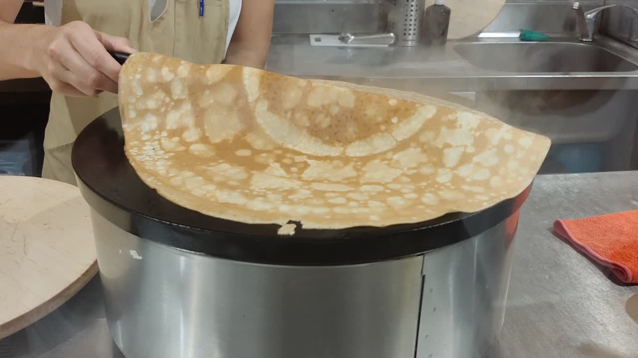 Woman's hands making, flipping pancakes french crepes from a pan on the gas stove and putting it aside in the plate