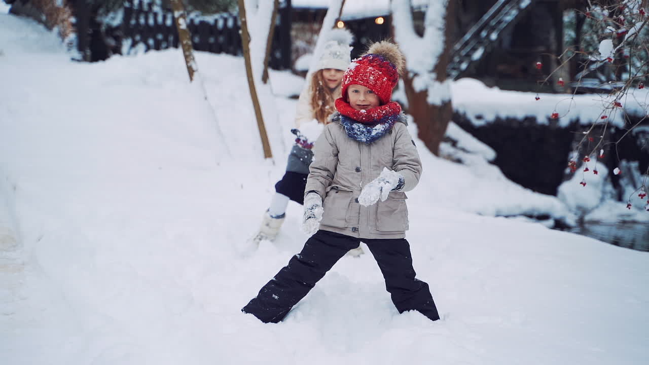 Beautiful snowball falling on a boy who is standing in snow. Cheerful children are throwing soft snow in winter. Little kids are playing happily with white snow. Slow motion.