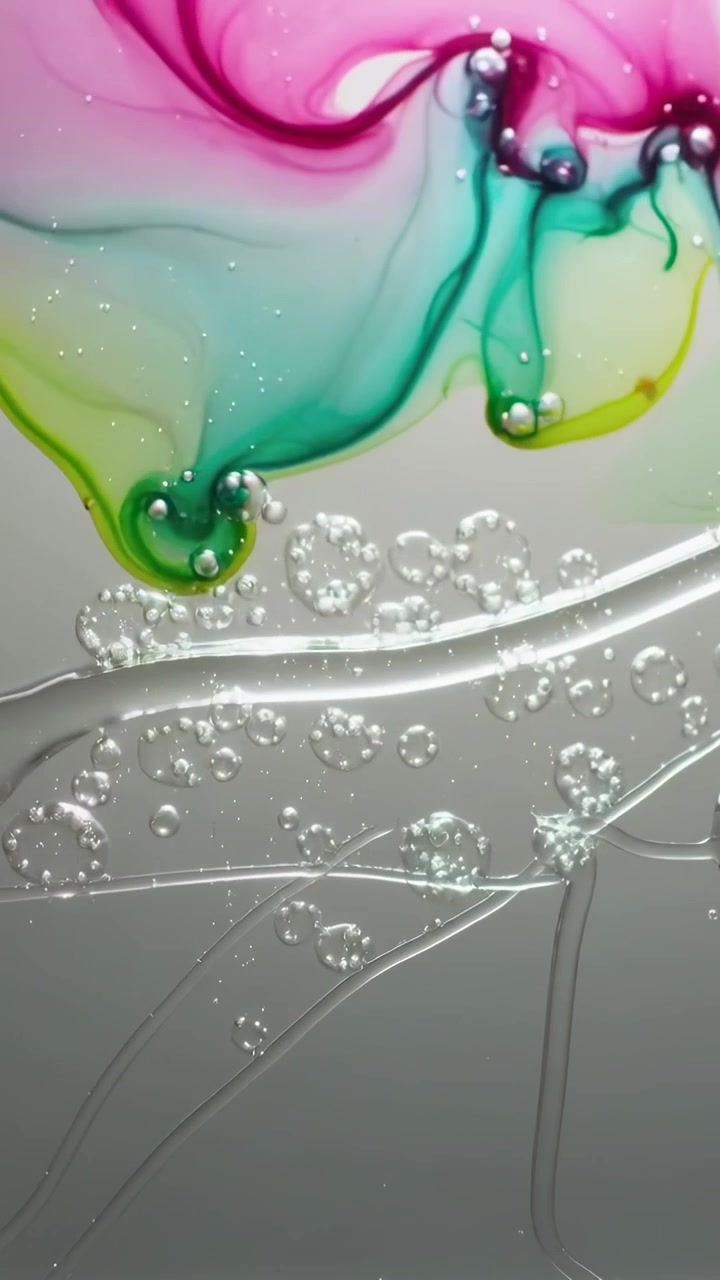 Vídeo vertical: Pigmentos rosa e azul-petróleo se espalhando e tocando resina em um painel cinza, formando bolhas.