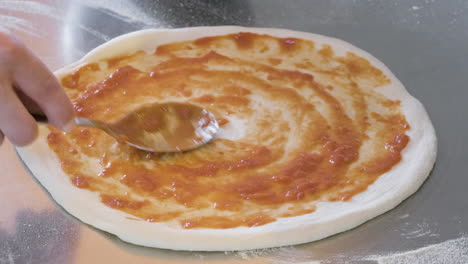 Close-Up-Of-An-Unrecognizable-Chef-Spreading-Tomato-Sauce-With-Spoon-On-The-Pizza-Raw-Dough-At-Restaurant-1