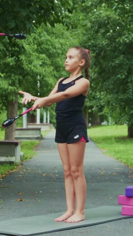 young child practicing fitness routine outdoors with resistance band in a green park setting, demonstrating physical strength and graceful movements