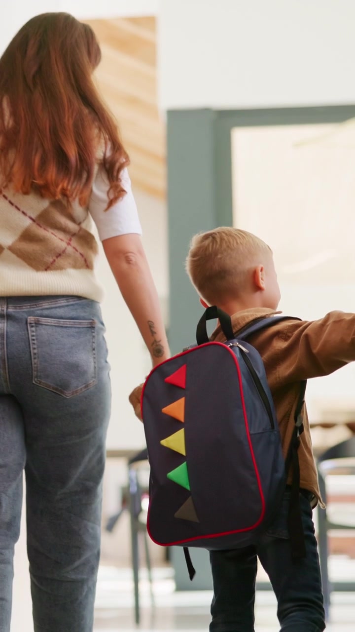 Mother Holding Hands With Young Son Wearing Backpack Walking Indoors