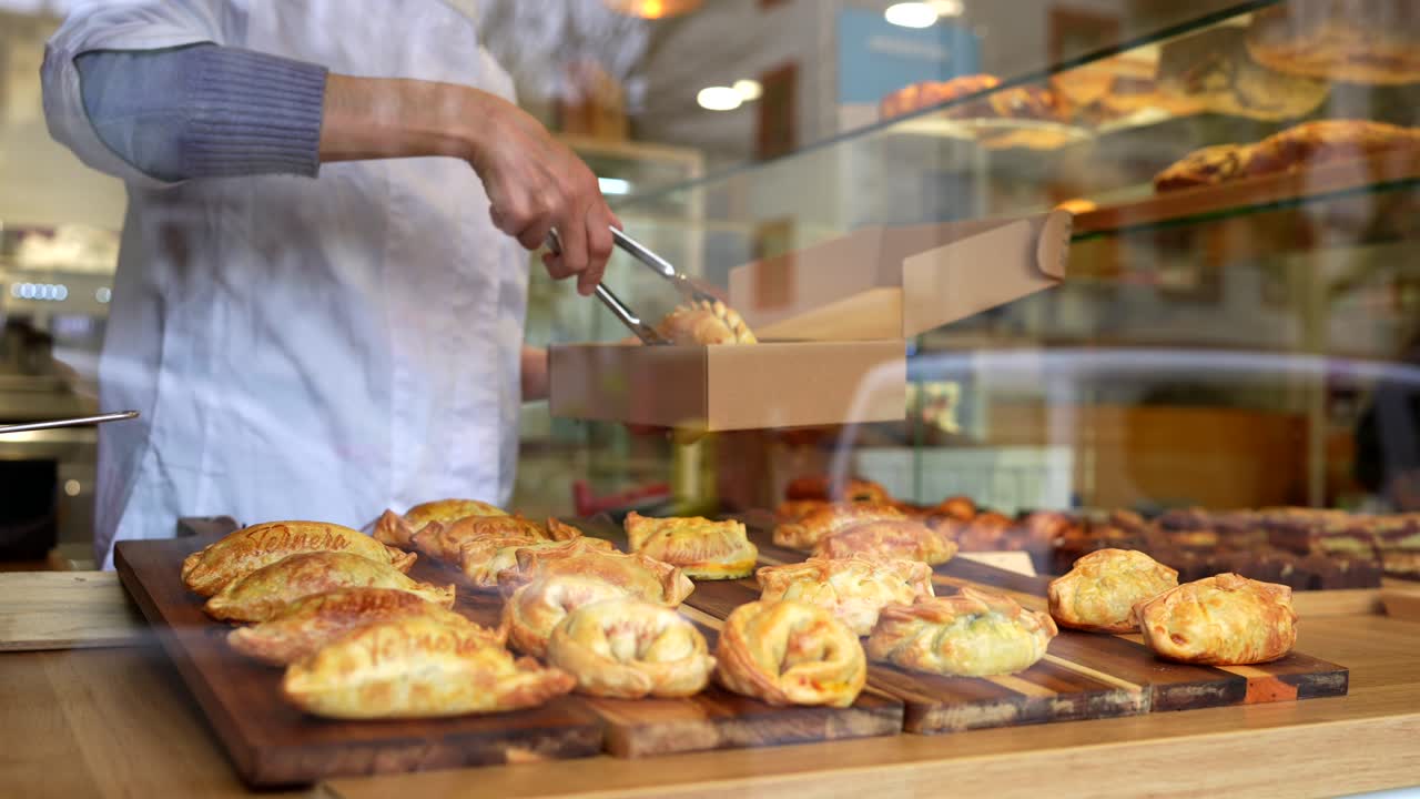 Padeiro servindo empanadas frescas em uma caixa para viagem em um café.