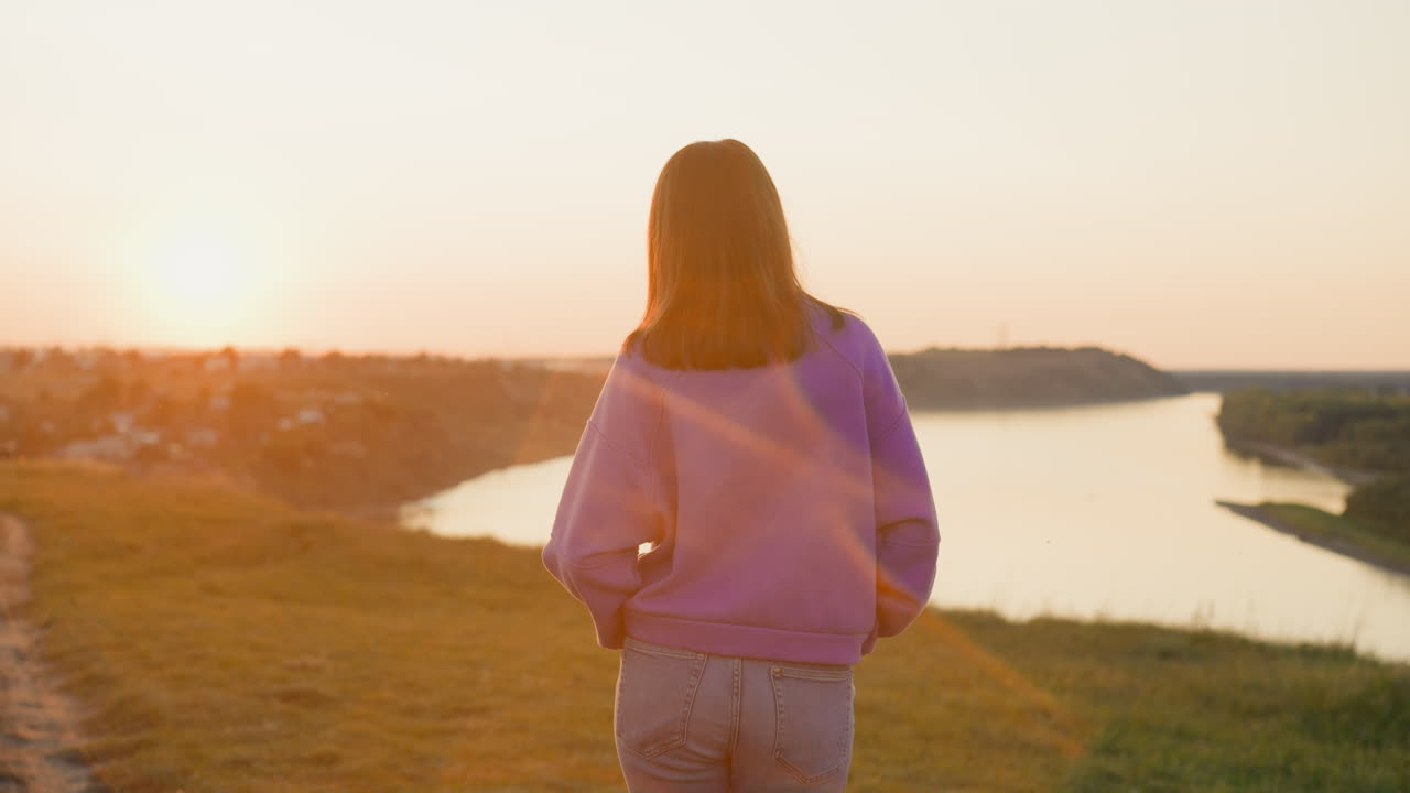 한 여인이 어두워지면서 강변을 혼자 산책하고 있다: 사려 깊은 여인은 평온한 봄 저녁을 즐기며 시골에서 산책한다.