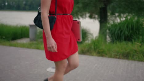 detail shot of attractive woman in red dress walking on the pavement in the park with a laptop in her hand