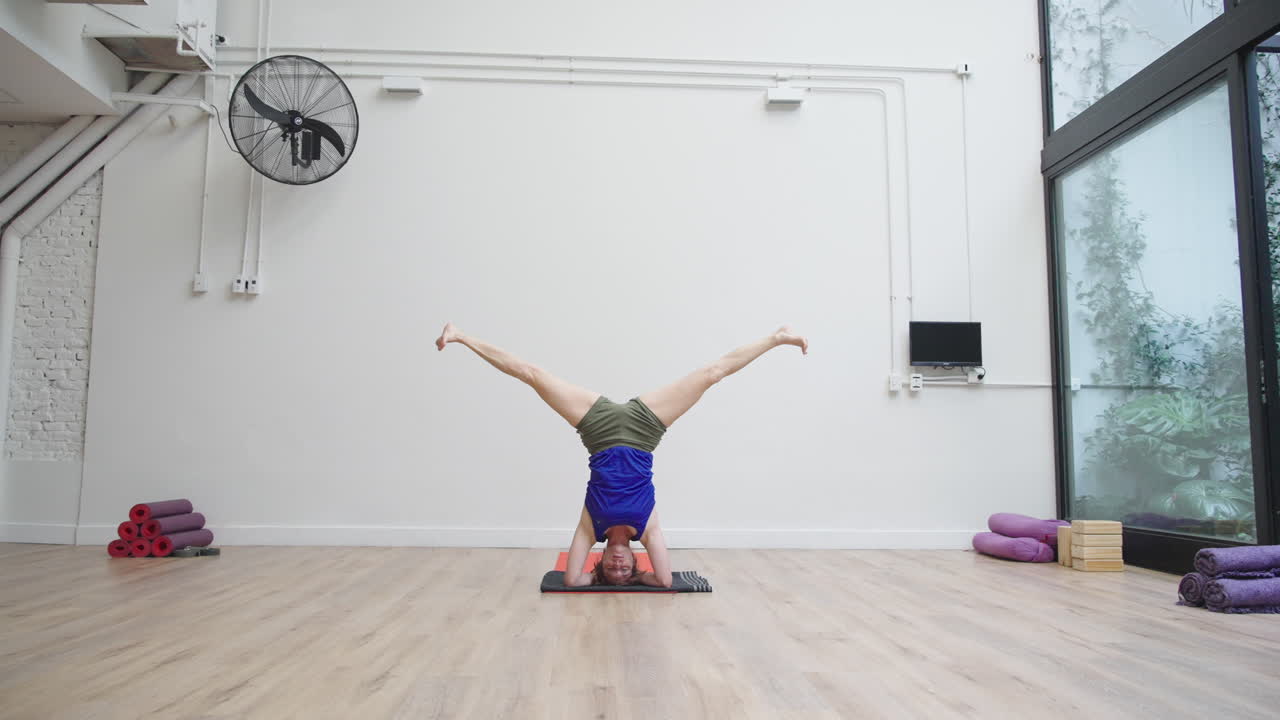 Donna che pratica una posizione yoga in verticale sulla testa in uno studio luminoso