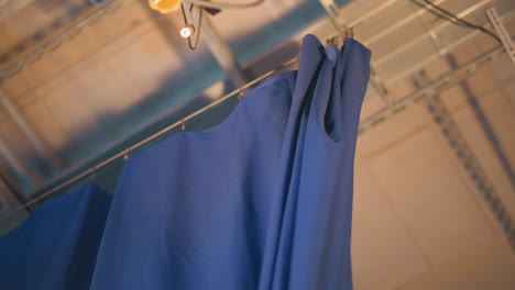 male operator pulls blue curtain inside television studio set during production setup, floor lights flare below, overhead rigging visible, revealing striped backdrop ready for live news recording