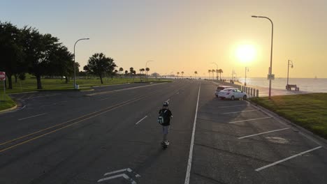 skateboarder riding on electronic skateboard with fiery sunset in lakeshore drive, new orleans, louisiana usa. aerial tracking