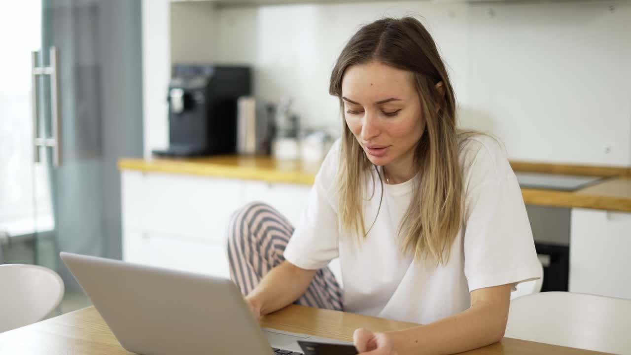 una mujer rubia está haciendo un pago en línea con una tarjeta bancaria usando una computadora portátil moderna en casa