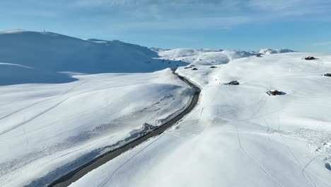 Road-RV-13-crossing-Vikafjell-mountain-in-western-norway---Sunny-day-aerial-flying-above-snow-covered-landscape