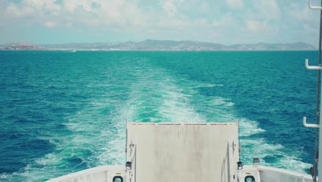 View-of-the-Mediterranean-Sea-from-the-back-of-a-ferry,-observing-the-ship-breaking-through-the-waves-and-leaving-the-island-of-Ibiza-behind