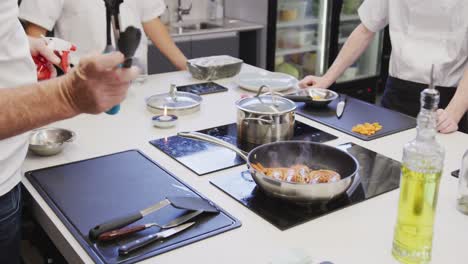 professional caucasian male chef in a restaurant kitchen preparing shrimps using a frying pan